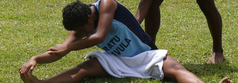 Two teenagers do stretching exercises at a track & field coaching session. Training exercises at a Sports placement abroad.